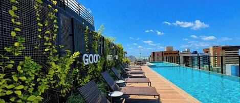 Un área de piscina en la azotea con sillones de descanso y una pared de vidrio con vegetación.