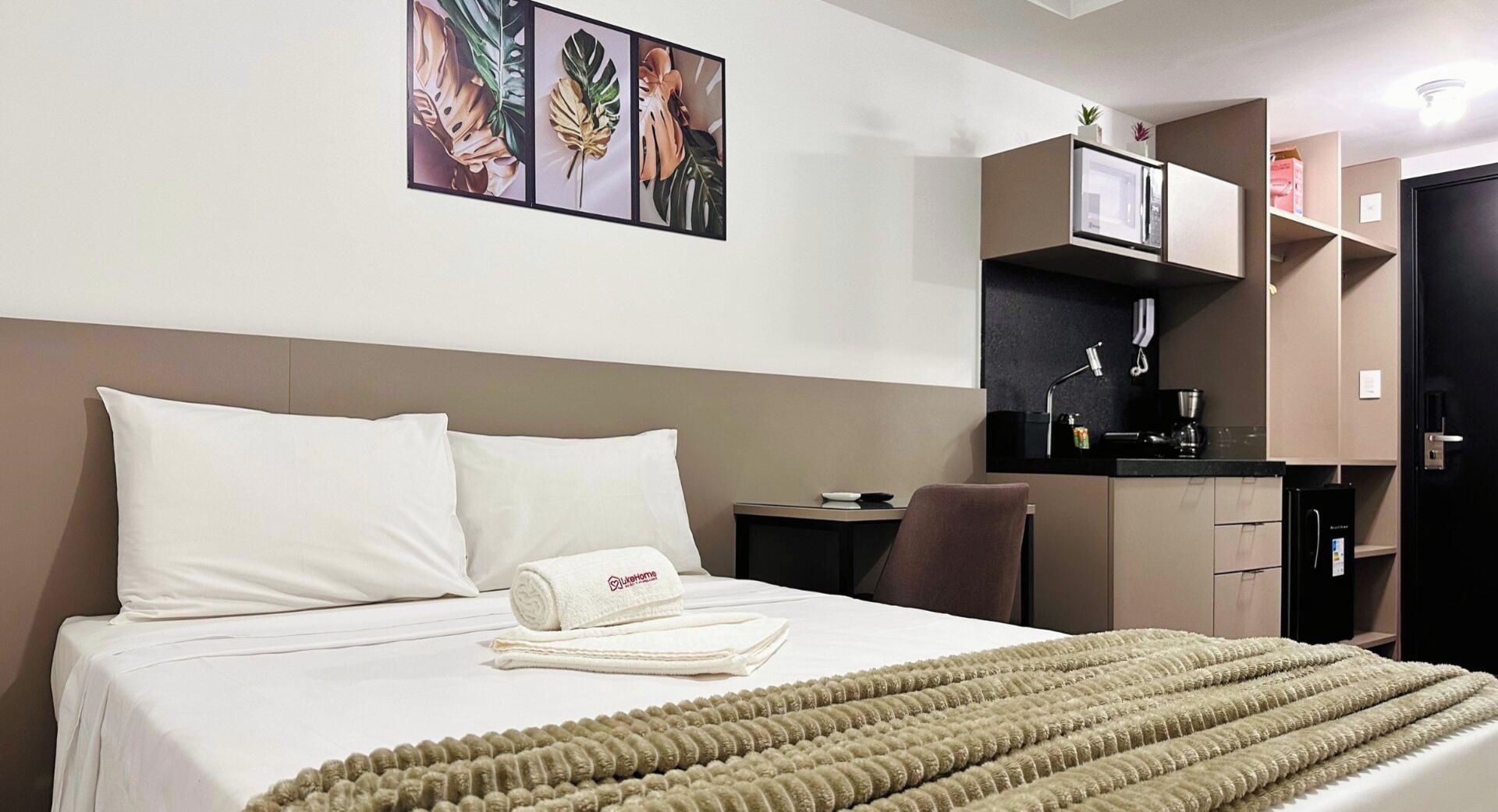 A hotel room with a bed, a desk, a chair, a microwave, and a refrigerator.