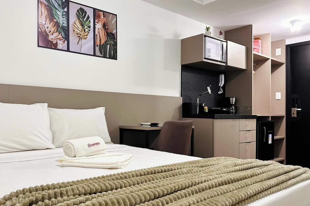 Una habitación de hotel con cama, escritorio, silla, microondas y refrigerador.