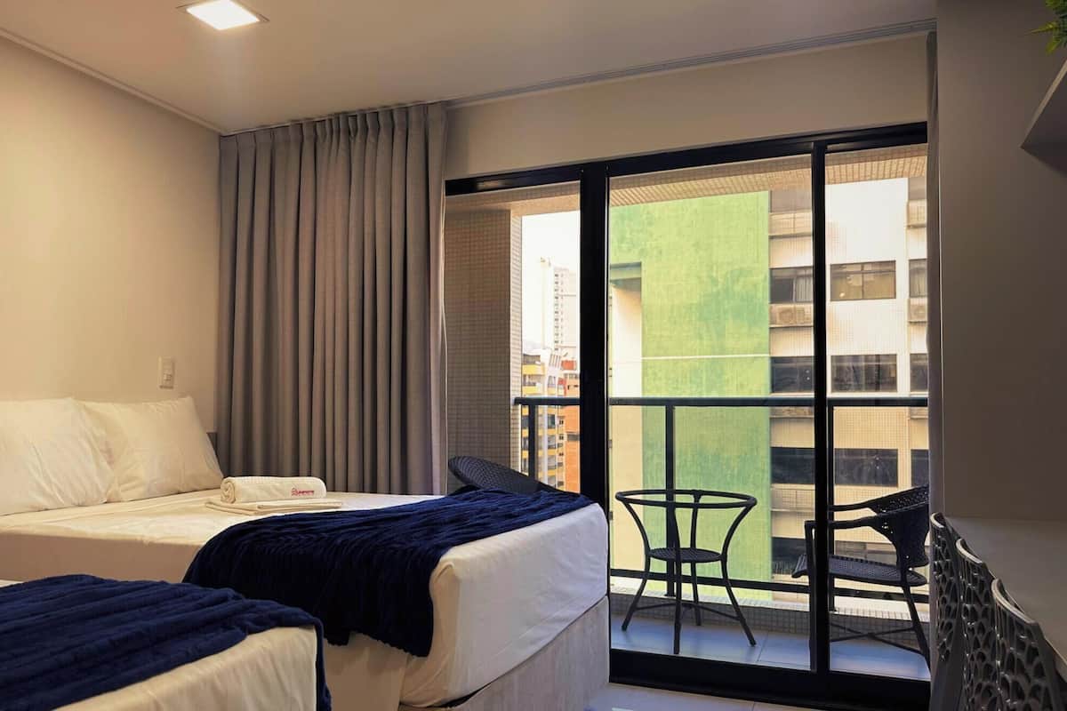 Habitación de hotel con dos camas, un balcón con una silla y vistas a la ciudad.