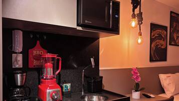 A kitchenette with a red blender, a coffee maker, a microwave, and a hanging light bulb.