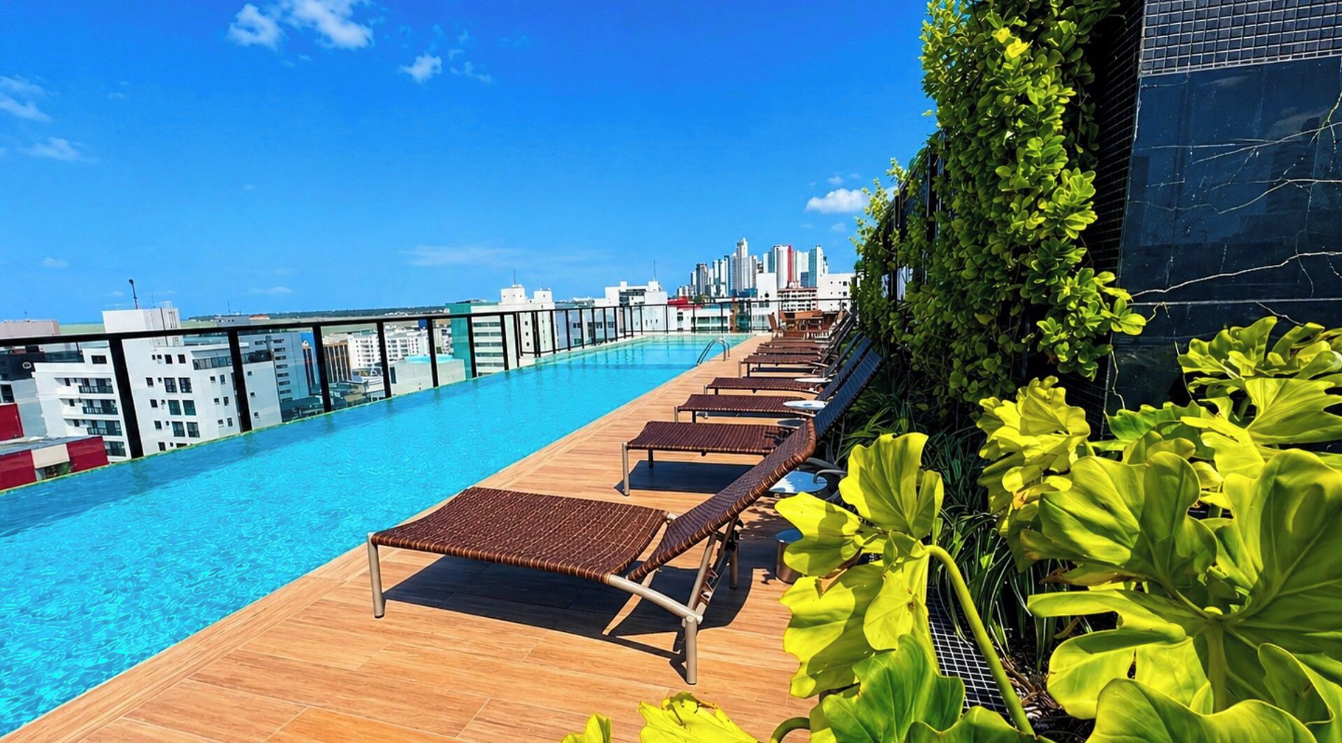 Piscina no terraço com espreguiçadeiras e vista para a cidade.