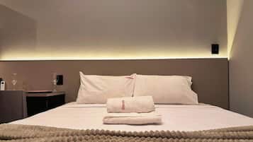 Ein Hotelzimmer mit einem ordentlich bezogenem Bett, einem Nachttisch mit einem Glas Wasser und einer Fernbedienung.