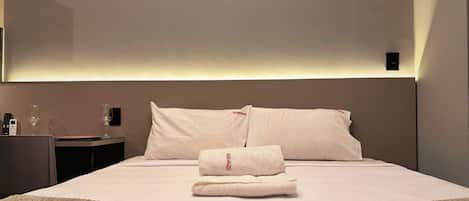 Una habitación de hotel con una cama bien hecha, una mesita de noche con un vaso de agua y un control remoto.