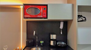 Een kleine keuken met een rode magnetron, een koffiezetapparaat, een waterkoker en een vuilnisbakje.