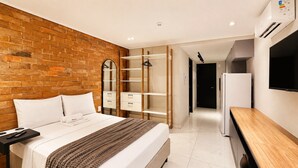 Una habitación de hotel moderna con una pared de acento de ladrillo, una cama grande con un plaid marrón, un escritorio de madera y un televisor de pantalla plana.