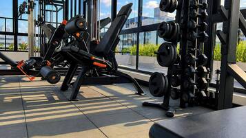 Ein Fitnessstudio mit verschiedenen Trainingsgeräten, großen Fenstern und Blick ins Freie.