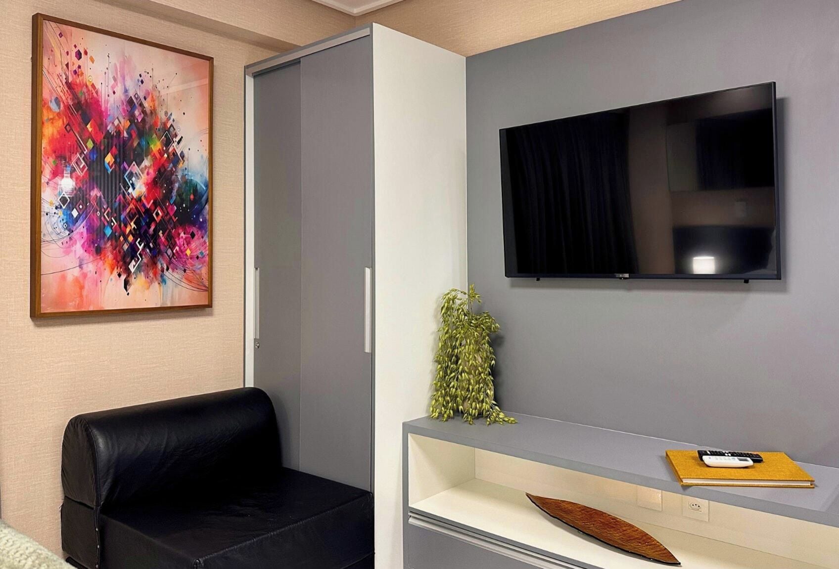 A modern living room with a black leather sofa, a flat-screen TV mounted on the wall, and a colorful abstract painting on the wall.
