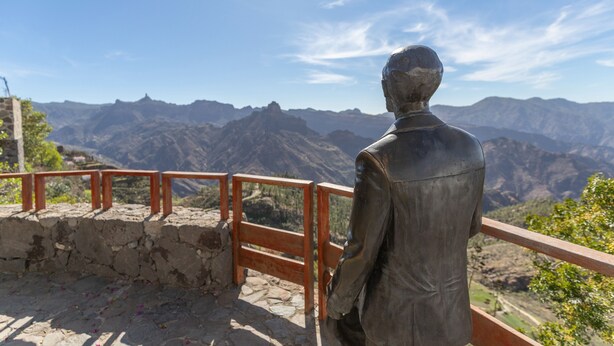 Estátua de um homem com vista para uma paisagem montanhosa.