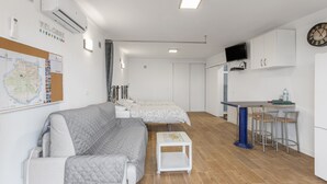 Um espaço compacto com sofá, uma mesa pequena, cozinha compacta e televisão fixada na parede.