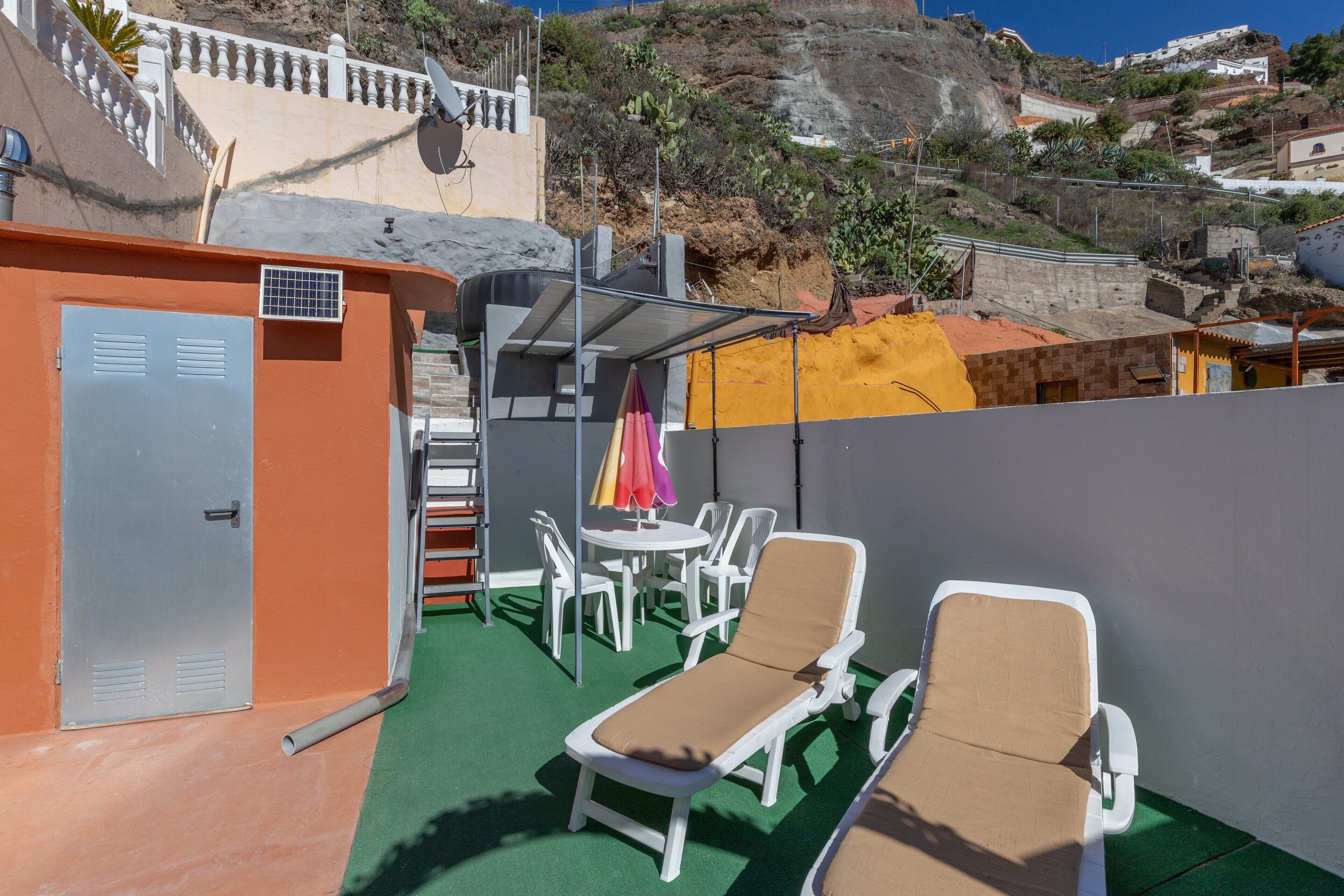 Une terrasse sur le toit avec deux chaises longues, une table et des chaises, et un petit espace aménagé en jardin.