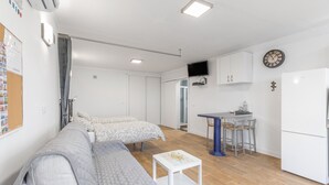 Espaço compacto para viver, com sofá, mesa pequena, cozinha compacta e TV na parede.