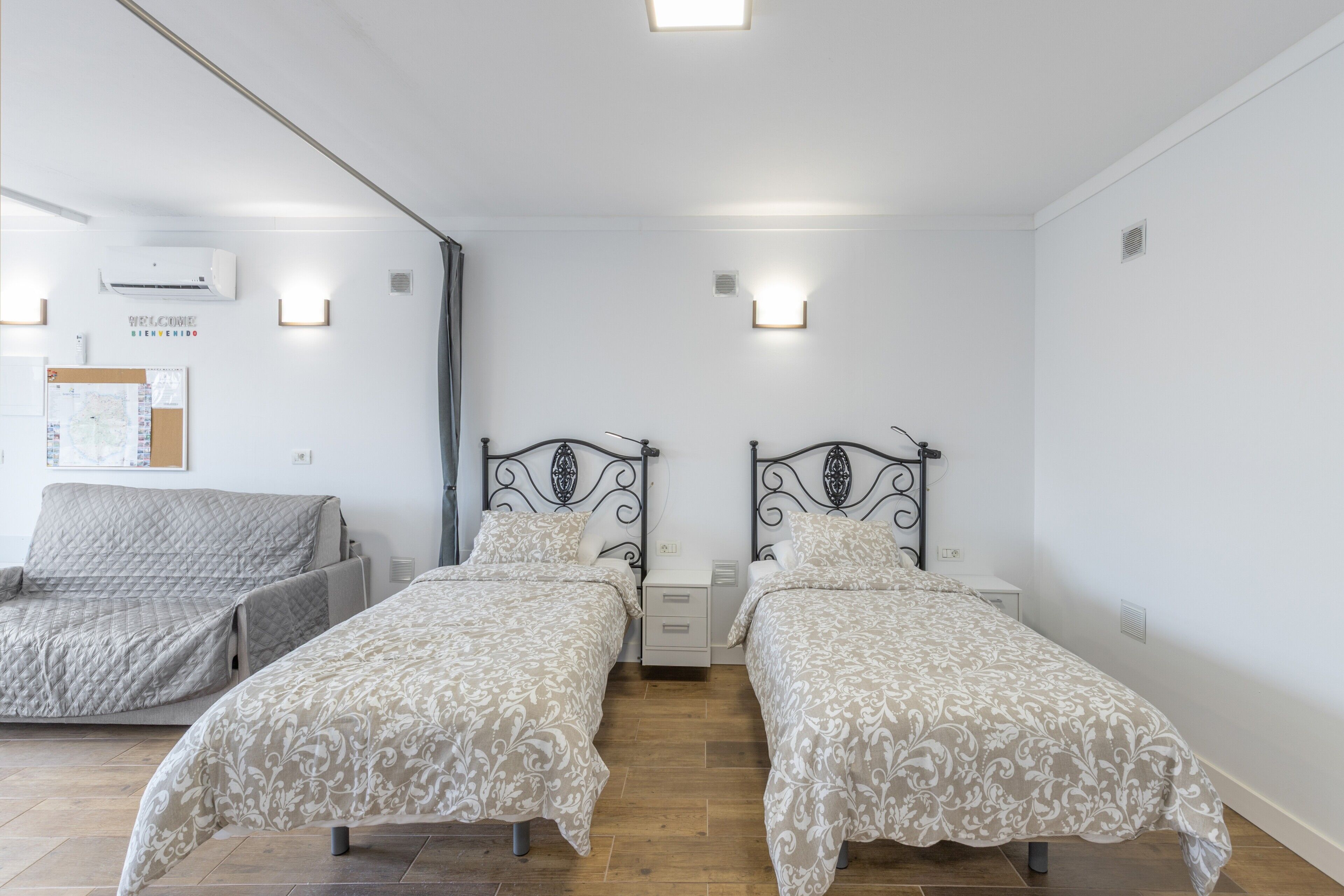 A room with two beds, a sofa, a wall-mounted air conditioner, and a bulletin board.