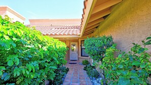 A pathway leading to a house with a tiled roof, surrounded by lush greenery and a stone wall. - 2 Bedroom at Woodhaven Country Club in Palm Desert. (Palm Desert)