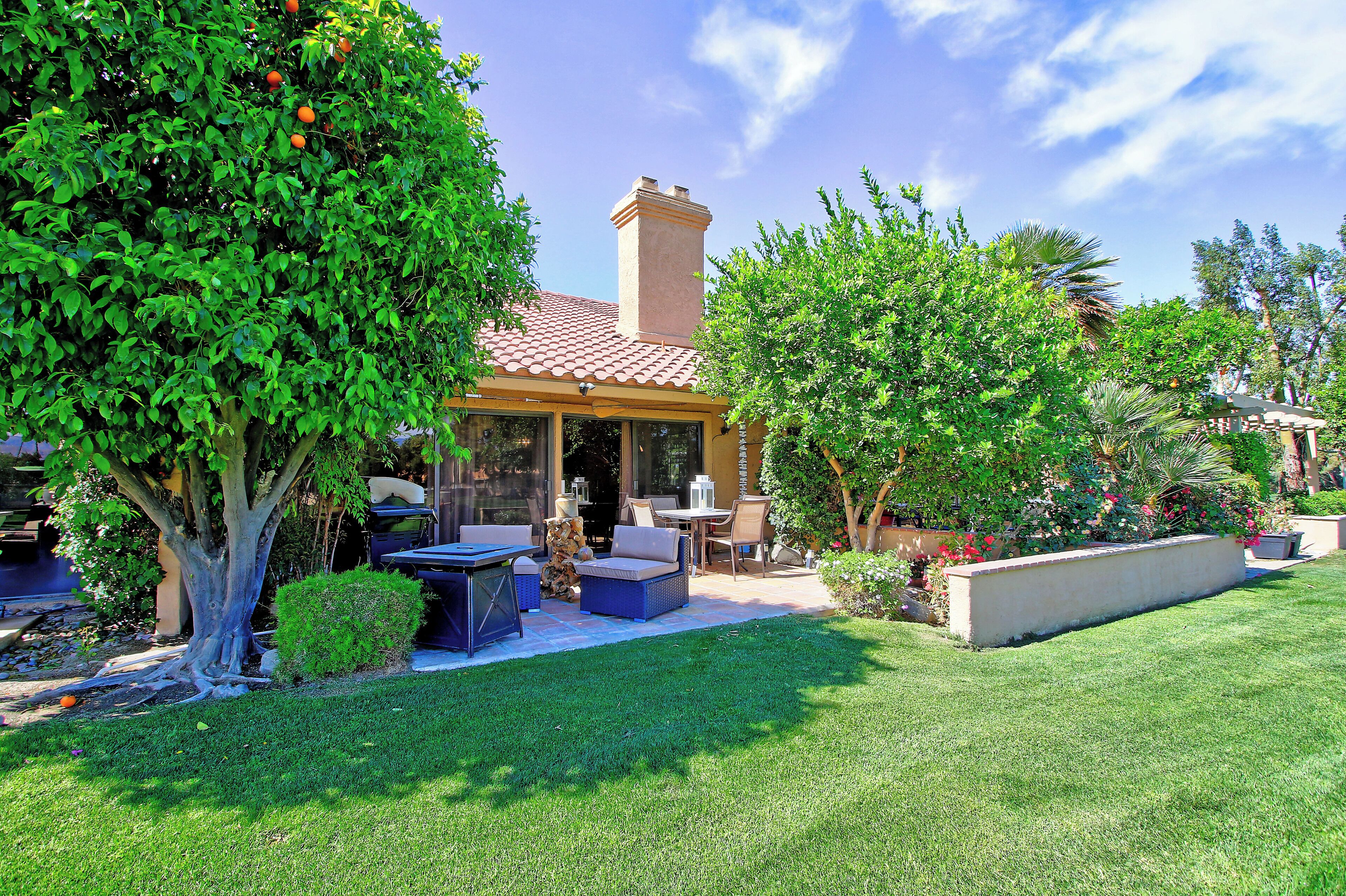 Un patio con mobiliario exterior, una zona de estar techada y un césped bien cuidado.