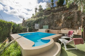 Ein Pool mit Steinrand, eine Liege und ein kleiner Tisch.