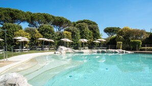 A clear swimming pool with rock formations, surrounded by trees and umbrellas. - Hotiday Lodge Viareggio (Viareggio)