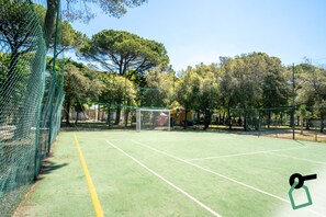 Un court de tennis avec un filet, entouré d’arbres et d’une clôture.