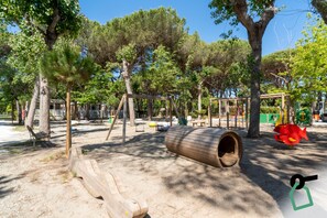 Une aire de jeux avec des balançoires, un toboggan en forme de tronc d’arbre et une structure en bois.