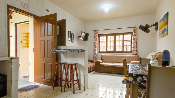 A cozy kitchen with a dining area, a sofa, and a window with curtains. - Cozy house in Balneário Jussara, Mongaguá. Just 600m from the beach. Pets allowed. (Mongaguá)