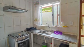 A compact kitchen with a gas stove, oven, sink, and window with a view of greenery. - Cozy house in Balneário Jussara, Mongaguá. Just 600m from the beach. Pets allowed. (Mongaguá)