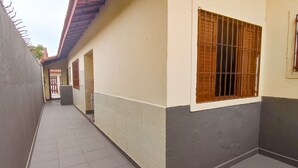 A narrow corridor with tiled flooring, a beige and gray wall, and a window with metal bars. - Cozy house in Balneário Jussara, Mongaguá. Just 600m from the beach. Pets allowed. (Mongaguá)
