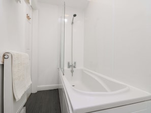 Un baño moderno con una bañera blanca, ducha con mampara de vidrio y una toalla colgada en la pared.