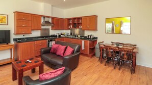 A modern kitchen with wooden cabinets, a dining area with a table and chairs, and a living room with a sofa and coffee table. - Farriers Cottage (Bridlington)