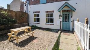 A two-story house with a front door, a small porch, and a wooden bench in the yard. - Farriers Cottage (Bridlington)