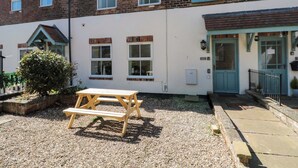 A two-story building with a brick facade, multiple windows, a wooden picnic table, and a gravel courtyard. - Chestnut Cottage (Bridlington)