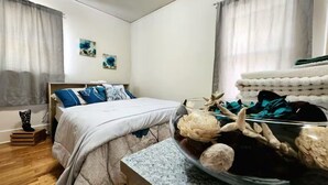 Ein Schlafzimmer mit einem Bett, einem Nachttisch, einer Glasvase mit Dekoration und einem Fenster mit Vorhängen.