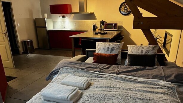 A bedroom with a bed, a bedside table, and a view of a kitchen area.