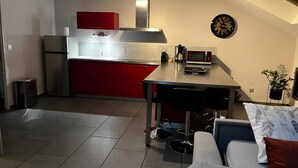 A compact kitchen with red cabinets, a stainless steel refrigerator, a microwave, and a coffee maker on the counter.