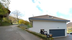 A single-story building with a garage, a small outdoor area with a table and chairs, and a paved driveway leading to the entrance.