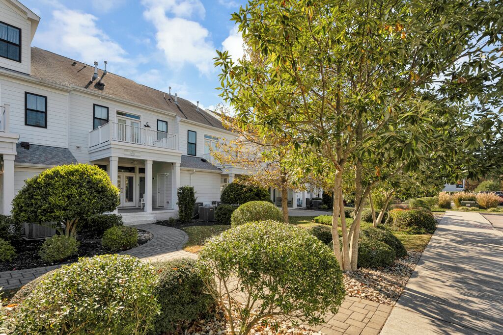 A two-story residential building with a front porch, a covered driveway, and well-maintained landscaping including hedges and trees.
