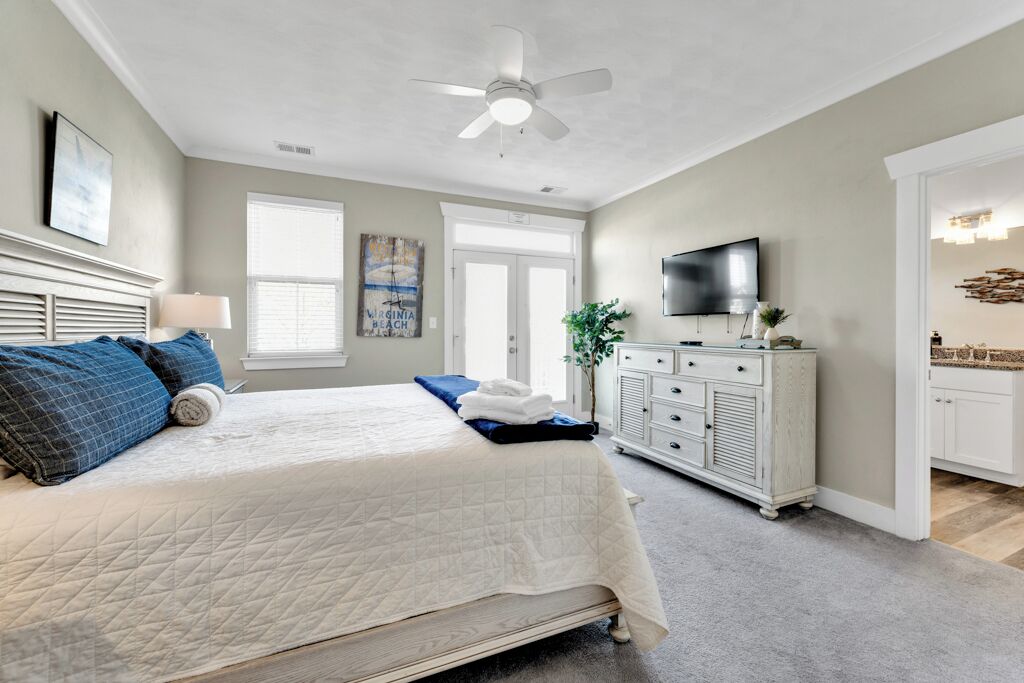 A bedroom with a bed, a dresser, a television, and a ceiling fan.