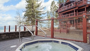 A hot tub with a view of the ocean, a wooden deck, and a building with balconies. - Relaxed Lakefront Living • Cozy 1BR Tahoe Condo (Tahoe Vista)