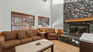 A cozy living room with a stone fireplace, a sofa, a chair, and a table with a remote control. - Relaxed Lakefront Living • Cozy 1BR Tahoe Condo (Tahoe Vista)
