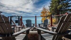 Une terrasse avec des fauteuils Adirondack, un foyer et une vue sur un lac et des montagnes.