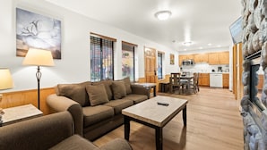 A living room with a sofa, a coffee table, and a lamp. There is a kitchen in the background with wooden cabinets and a microwave. - Where Lake Air Meets Fireplace Nights 2BR Condo (Tahoe Vista)
