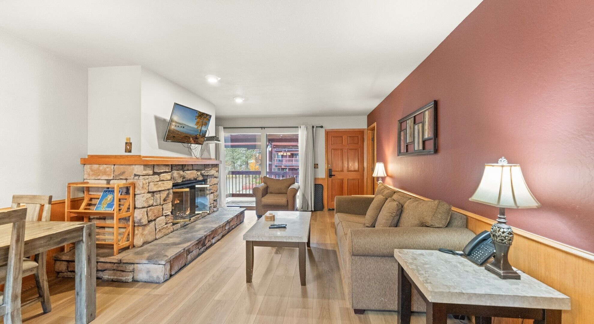A living room with a stone fireplace, a television mounted on the wall, a sofa, a coffee table, and a lamp.