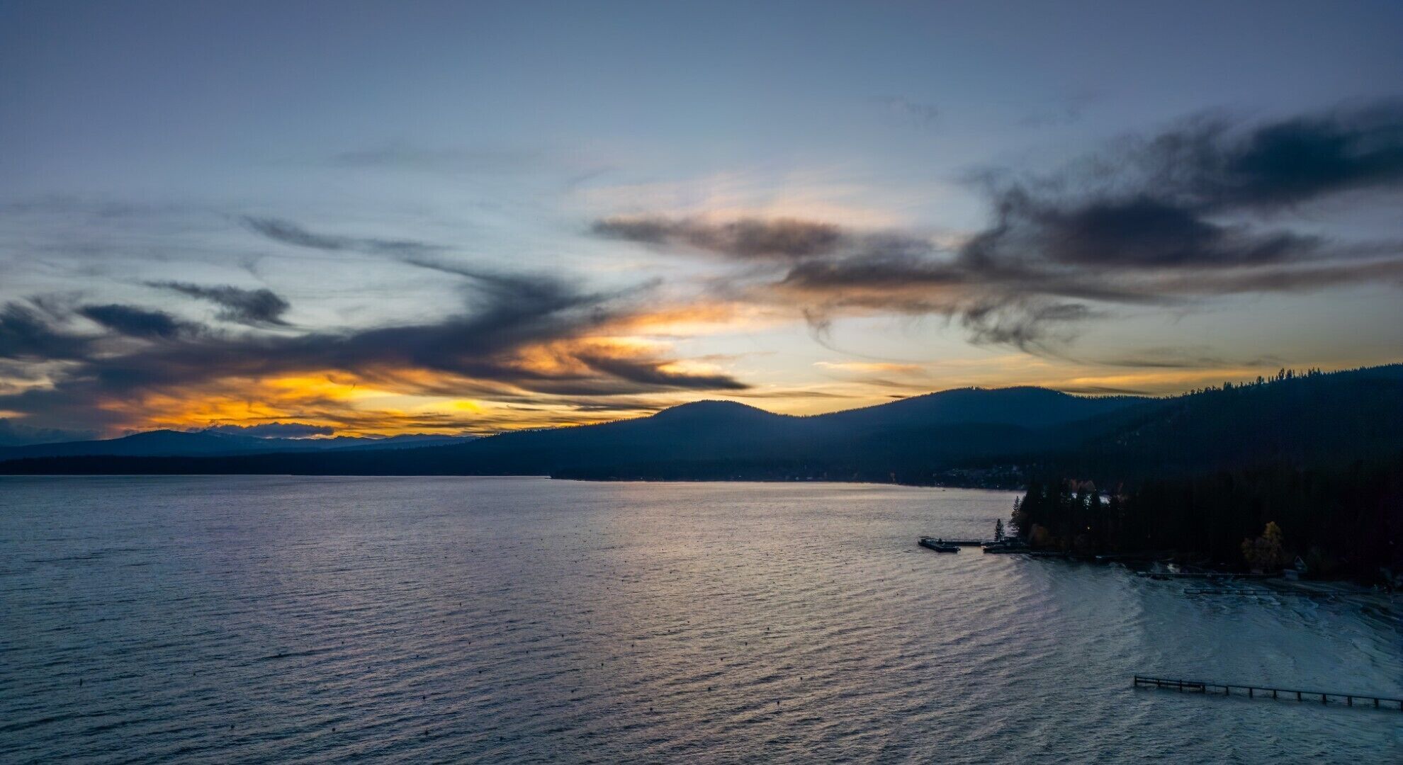 Ein See mit Bergen im Hintergrund und einem Sonnenuntergang.