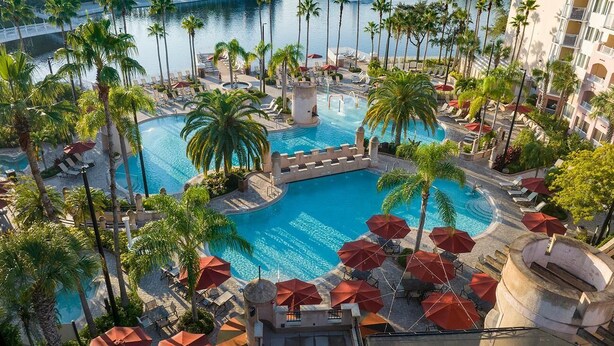 Ein Poolbereich eines Resorts mit mehreren Schwimmbecken, Palmen und Liegestühlen.