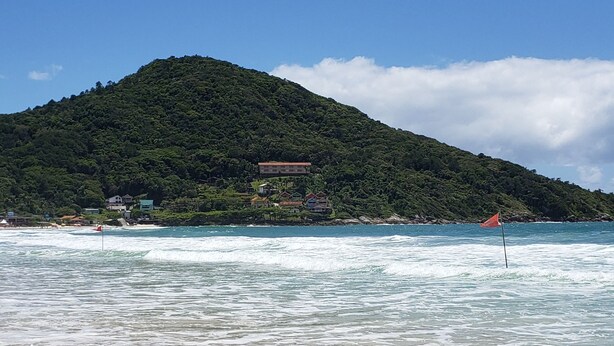 Une plage avec des vagues, une montagne en arrière-plan et un immeuble à plusieurs étages.