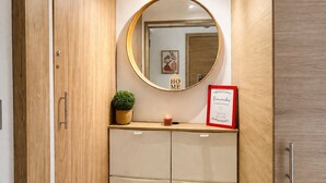 Un baño pequeño con tocador de madera, un espejo redondo, un cartel de bienvenida enmarco y una planta en maceta.