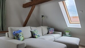 A modern living room with a grey sofa, colorful cushions, a floor lamp, a small potted plant, and a skylight. - Fewo am Kirchbrunnen (DG) - Quiet time out for 2 (Urspringen vor der Rhön)