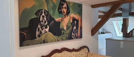 A living room with a large painting of two dogs and a woman, a wooden ceiling beam, and a patterned sofa.