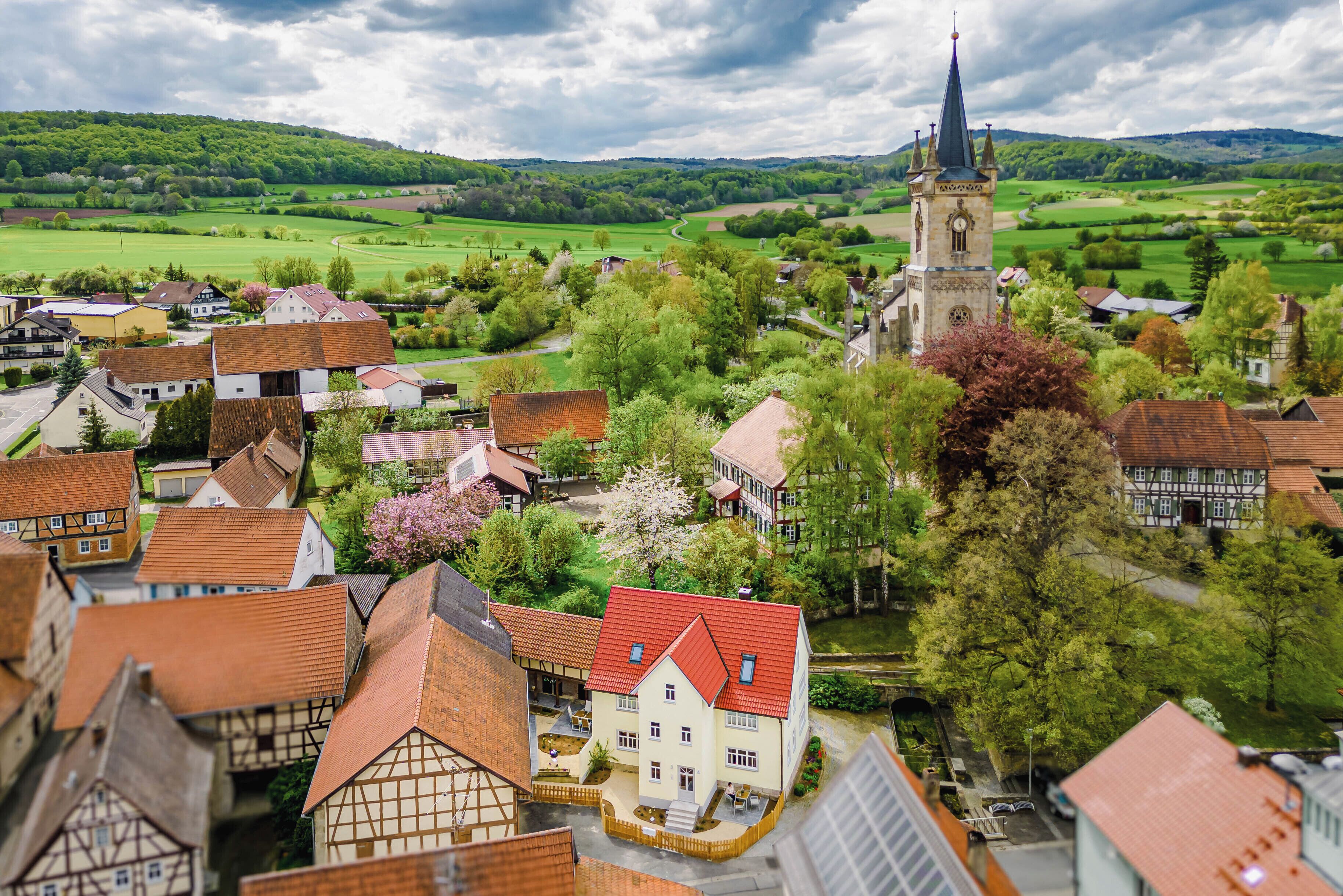 Une ville dotée d’une architecture traditionnelle, d’un clocher d’église imposant et entourée de champs verdoyants.