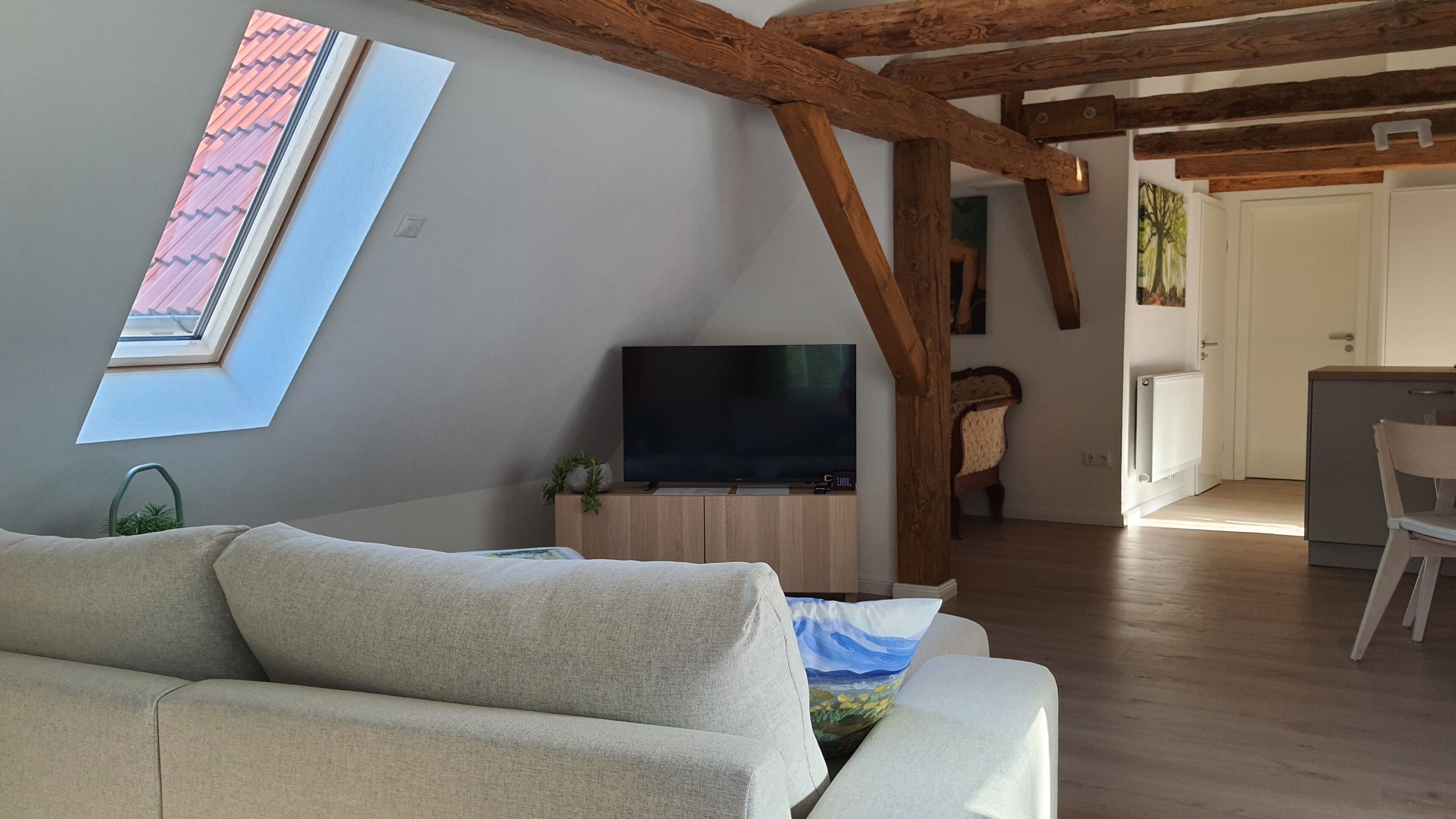Una sala moderna con sofá, televisor de pantalla plana, vigas de madera, tragaluz y vistas al exterior.