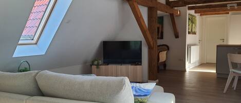 Una sala moderna con sofá, televisor de pantalla plana, vigas de madera, tragaluz y vistas al exterior.